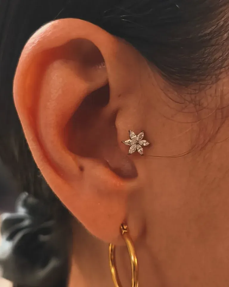 Perforación en el cartílago de la oreja con una joya en forma de flor, y un aro en el lóbulo