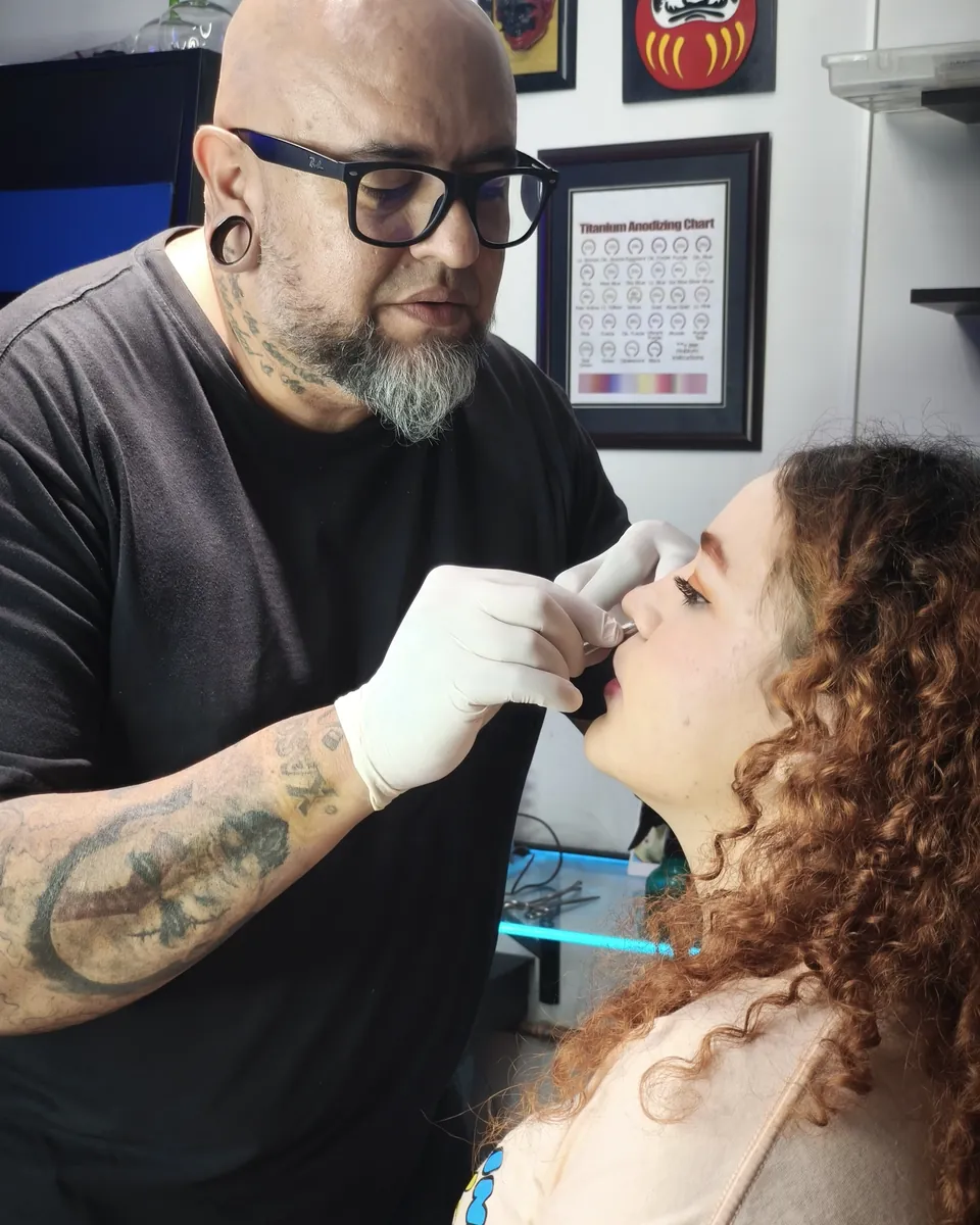 Kewyn perforando la nariz de una clienta con guantes y material estéril