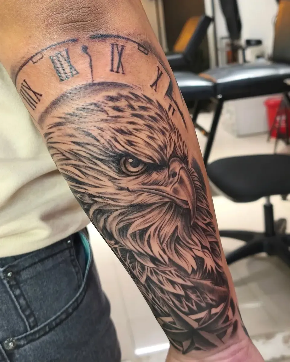 Tatuaje en realismo de un águila con un reloj de números romanos en el antebrazo